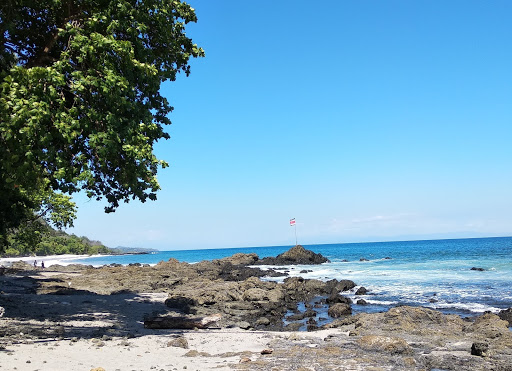 Plage de sable blanc du Costa Rica avec des rochers et des arbres